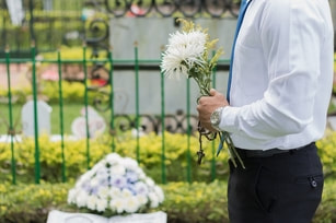 A male is holding flowers in front of a grave in a cemetarty