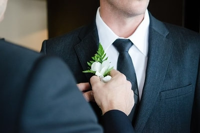 The best man putting a boutonniere on the groom.